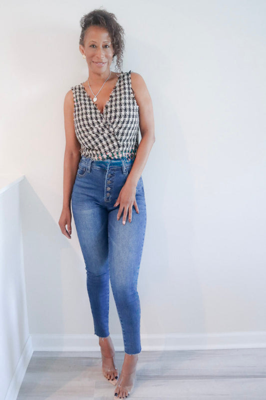 A woman modeling a sleeveless black and white houndstooth wrap top paired with high-waisted blue jeans, standing against a plain white wall.