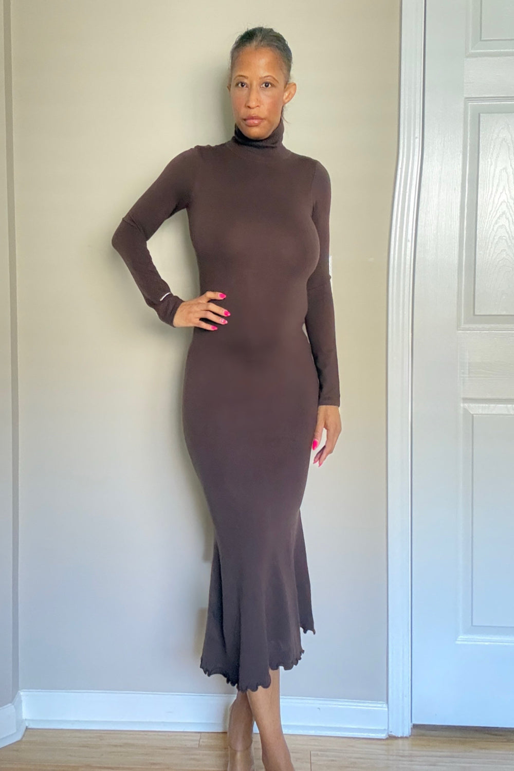 Woman wearing a brown dress standing against a neutral wall.