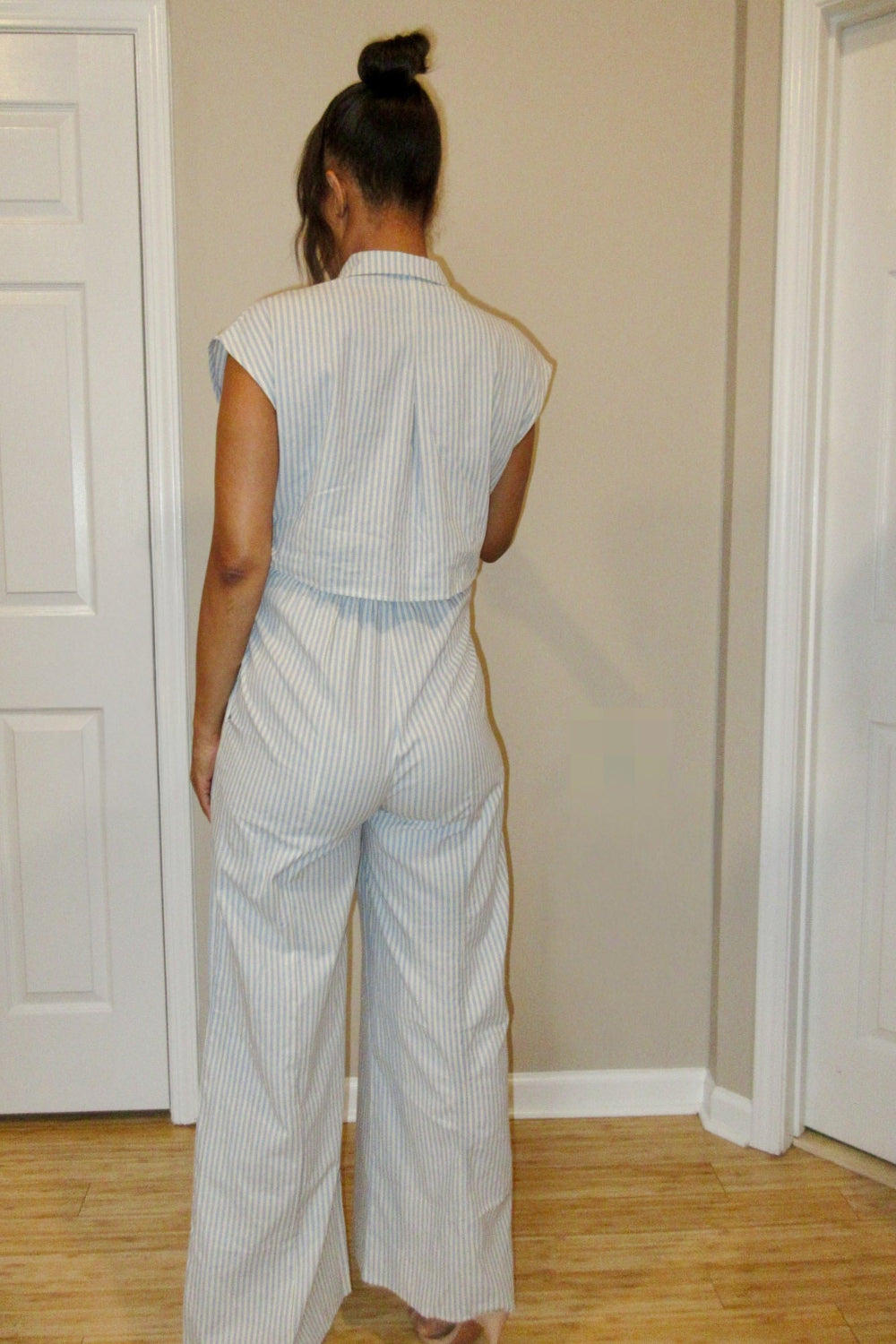 Person wearing a light blue and white striped outfit standing in a room with beige walls and wooden flooring.