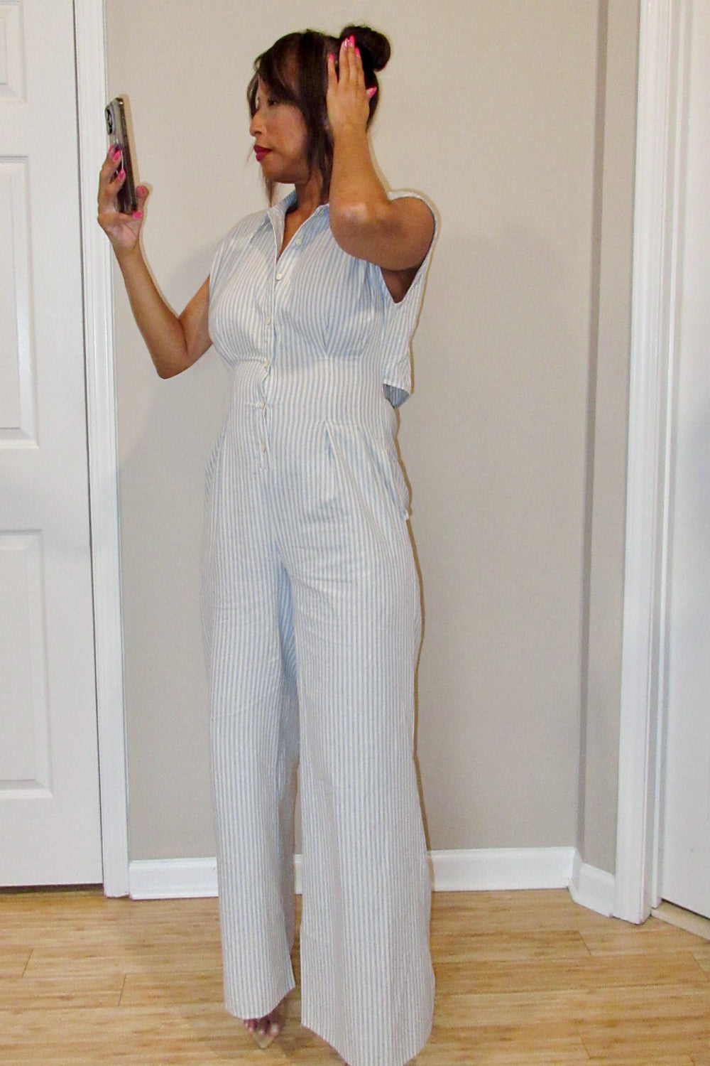 Woman taking a mirror selfie wearing a light blue striped jumpsuit.