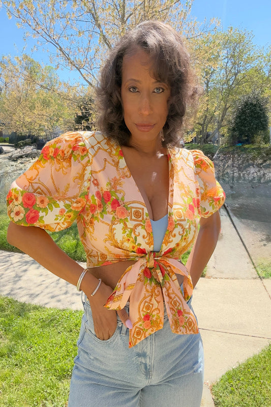 Woman wearing a floral blouse with a tie detail outdoors on a sunny day.