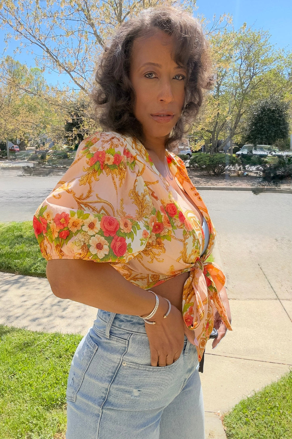 Woman wearing a floral blouse and high-waisted jeans standing outdoors.
