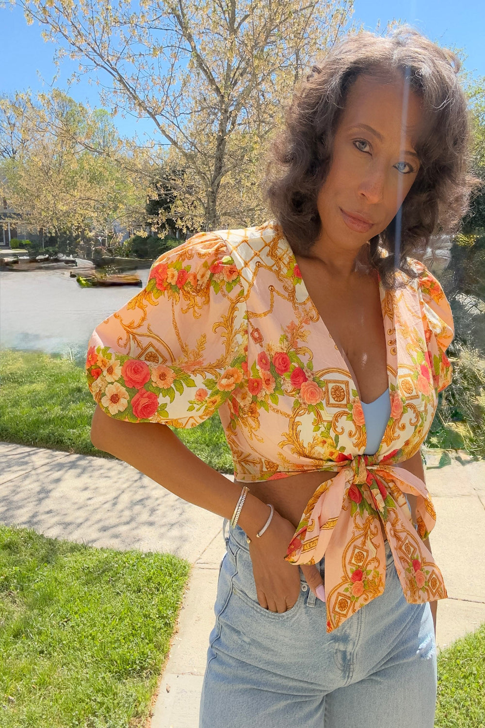 Woman wearing a floral blouse outdoors with trees and water in the background