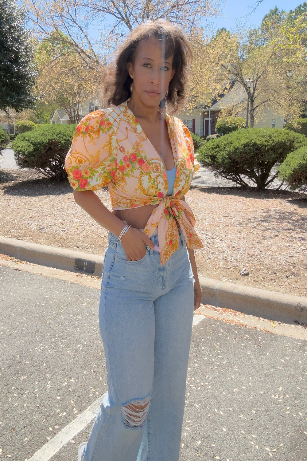 Woman wearing a floral top and light blue jeans standing on a street.