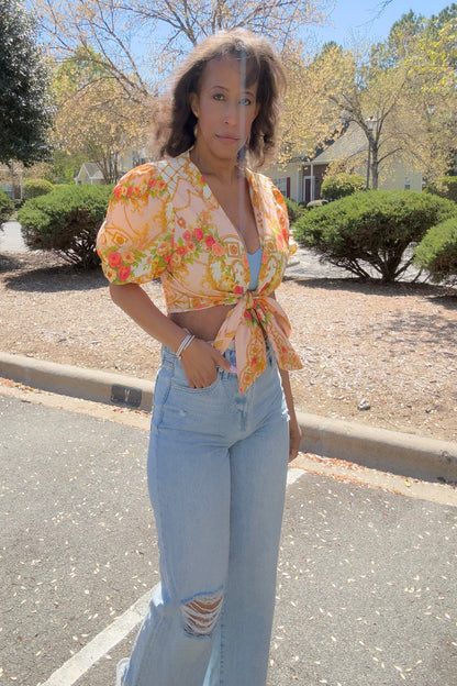 Woman wearing a floral top and light blue jeans standing on a street.